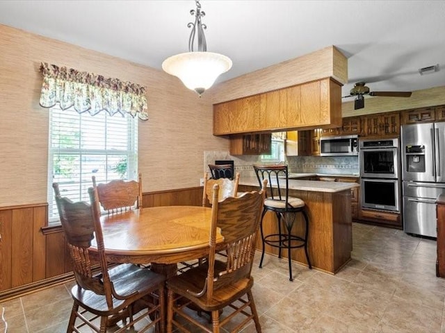 dining space featuring ceiling fan and wooden walls