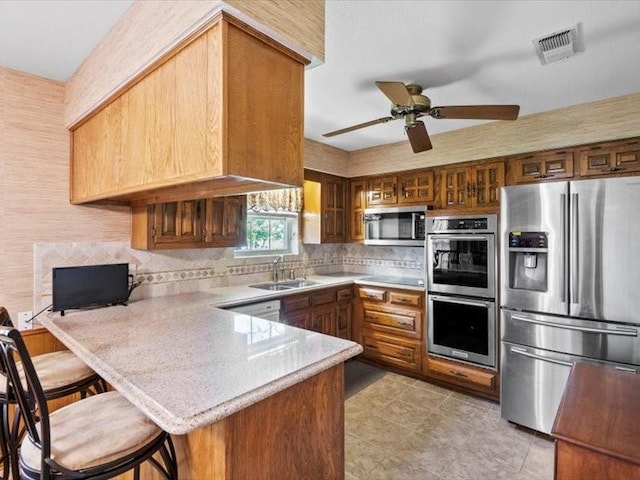 kitchen featuring kitchen peninsula, appliances with stainless steel finishes, a kitchen bar, ceiling fan, and sink