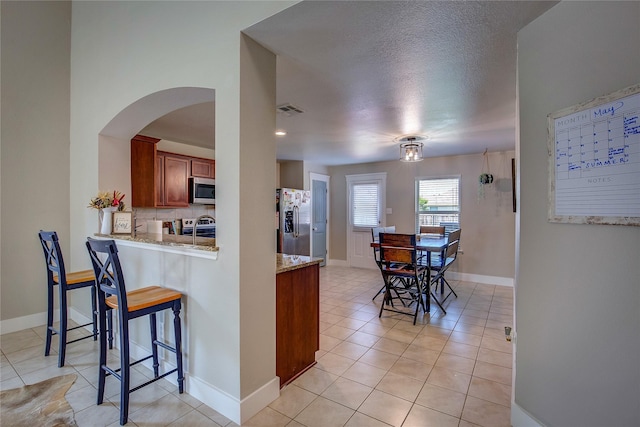 kitchen with light stone countertops, tasteful backsplash, a textured ceiling, stainless steel appliances, and light tile patterned flooring