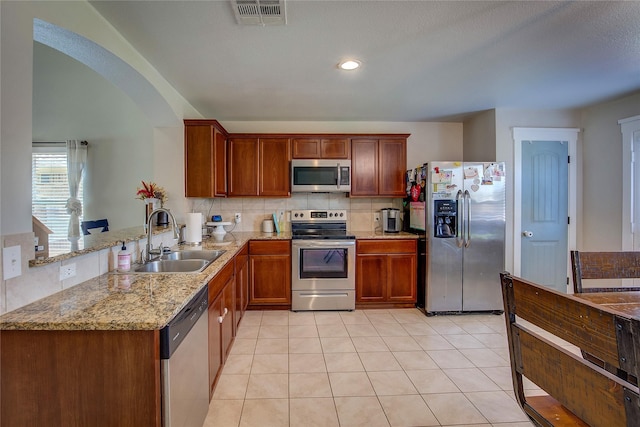 kitchen featuring light stone countertops, sink, backsplash, kitchen peninsula, and appliances with stainless steel finishes