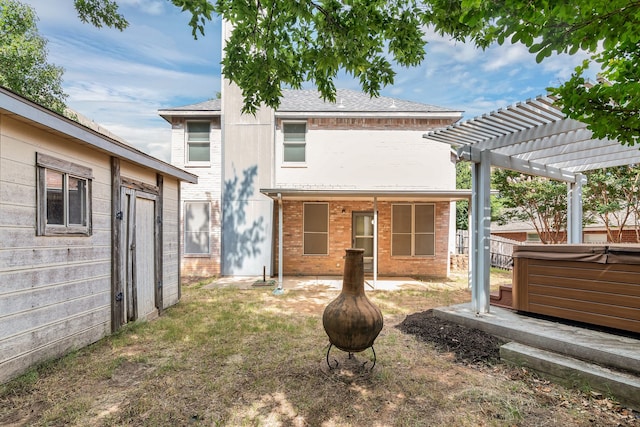 rear view of property with a pergola and a hot tub