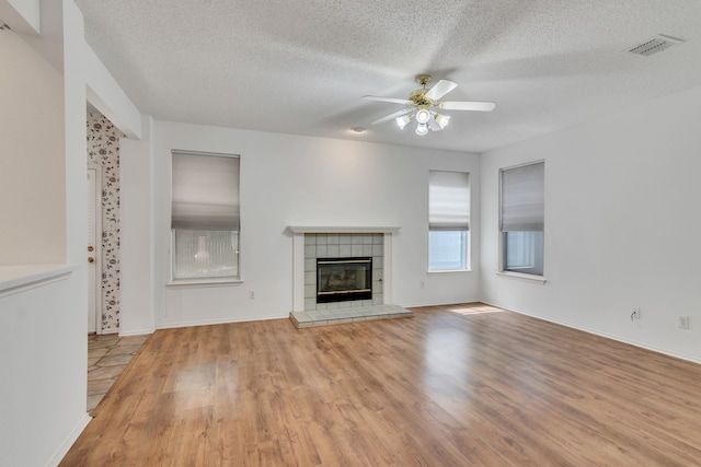 unfurnished living room with a tile fireplace, a textured ceiling, light hardwood / wood-style floors, and ceiling fan