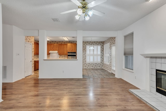 unfurnished living room featuring ceiling fan, light wood-type flooring, a textured ceiling, and a tile fireplace