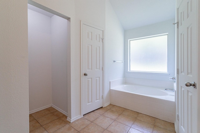 bathroom with a relaxing tiled tub, vaulted ceiling, and tile patterned floors