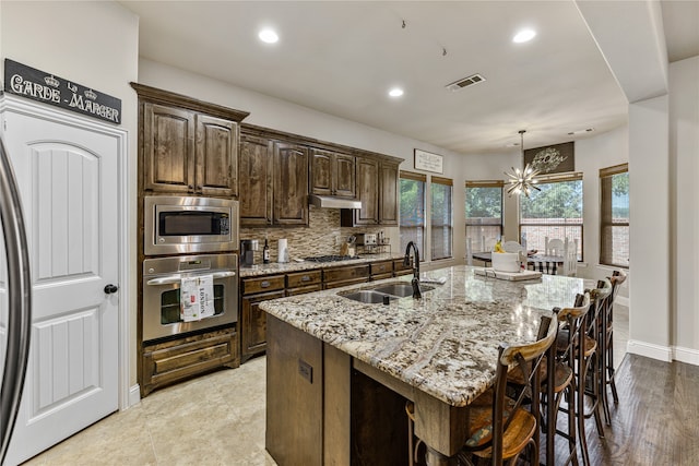 kitchen featuring light stone countertops, stainless steel appliances, sink, pendant lighting, and a center island with sink