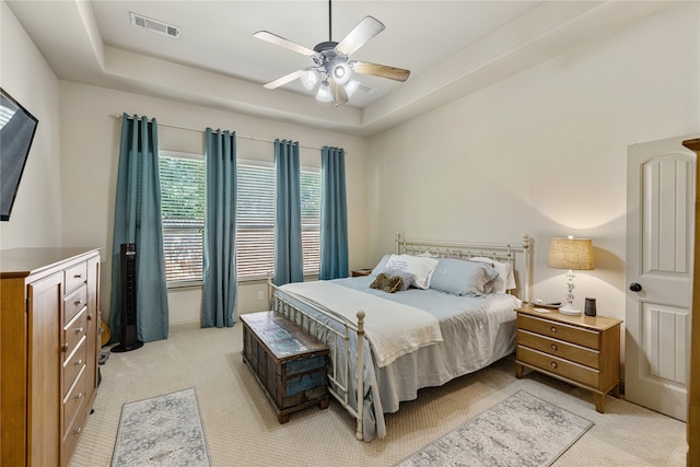 carpeted bedroom with a raised ceiling and ceiling fan