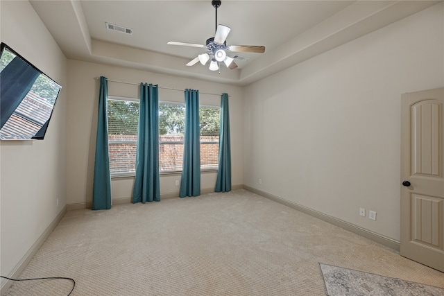 spare room with a raised ceiling, light carpet, and ceiling fan