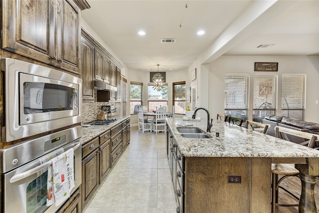 kitchen with sink, a kitchen breakfast bar, light stone counters, a center island with sink, and appliances with stainless steel finishes