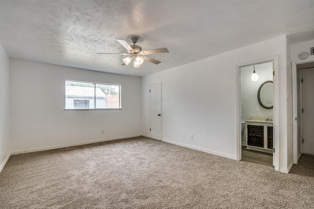 unfurnished bedroom featuring ceiling fan, carpet flooring, ensuite bath, and a textured ceiling