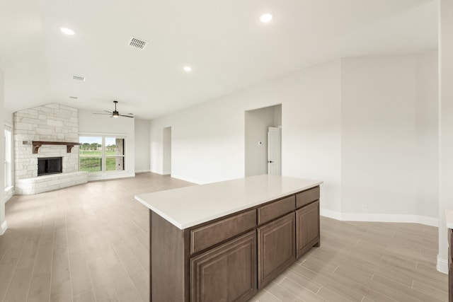 kitchen with a center island, vaulted ceiling, a fireplace, light hardwood / wood-style flooring, and ceiling fan