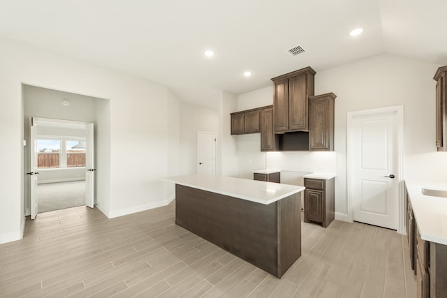 kitchen with dark brown cabinetry, light hardwood / wood-style flooring, lofted ceiling, and a center island