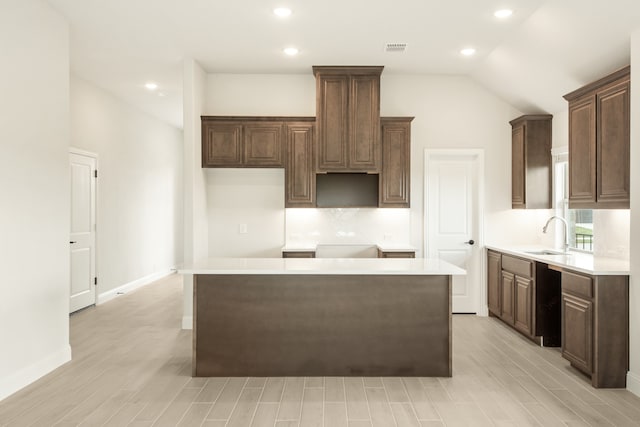 kitchen featuring light wood-type flooring, lofted ceiling, a kitchen island, and sink