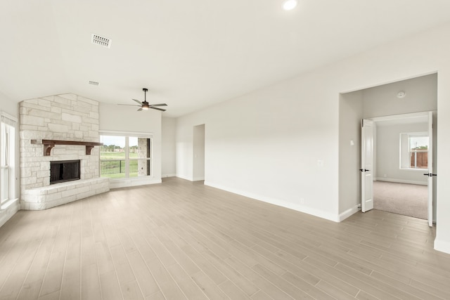 unfurnished living room featuring ceiling fan, a stone fireplace, and light hardwood / wood-style flooring