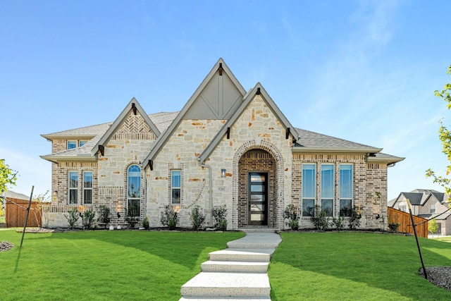 french country style house featuring brick siding, stone siding, fence, and a front yard