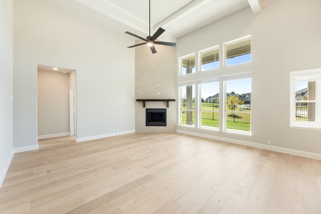 unfurnished living room featuring beam ceiling, a large fireplace, ceiling fan, a towering ceiling, and light hardwood / wood-style floors