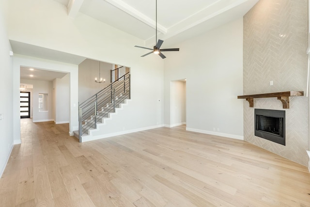 unfurnished living room featuring high vaulted ceiling, a tiled fireplace, light wood-style flooring, stairs, and beamed ceiling