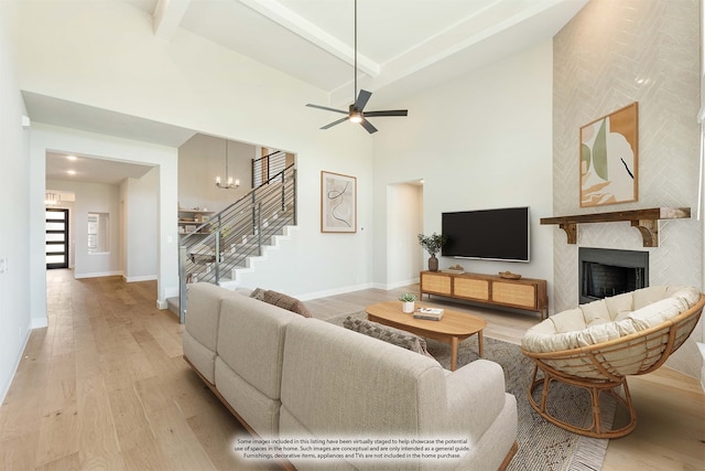 living room featuring beamed ceiling, light hardwood / wood-style flooring, ceiling fan with notable chandelier, a large fireplace, and high vaulted ceiling