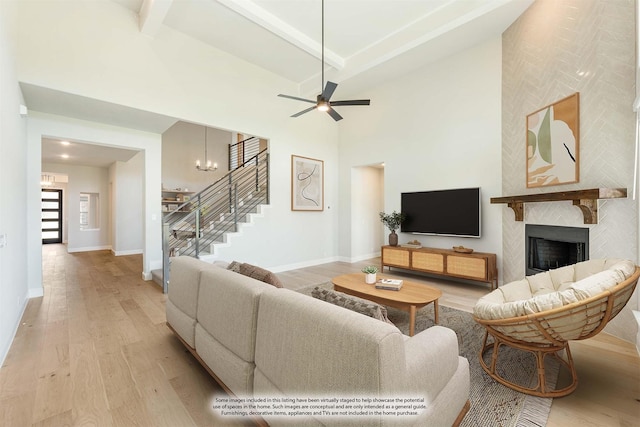 living area with stairs, high vaulted ceiling, a large fireplace, and light wood-style flooring