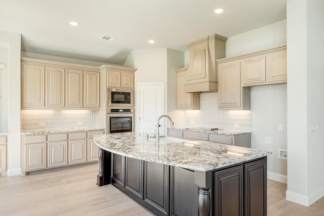 kitchen featuring premium range hood, cream cabinets, black appliances, and visible vents