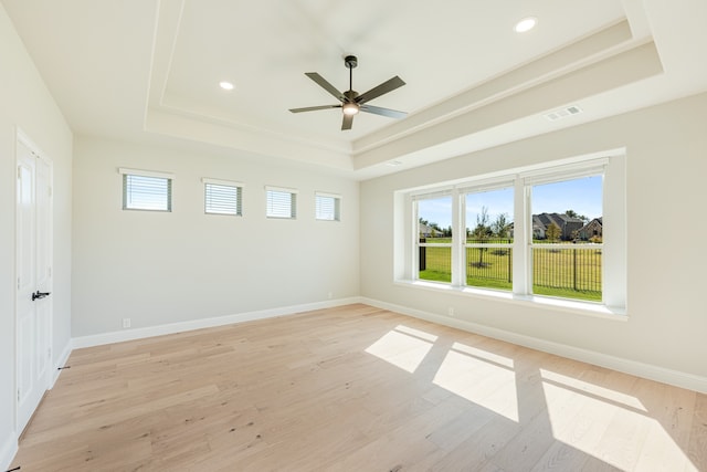 empty room with a tray ceiling, light wood-type flooring, and ceiling fan