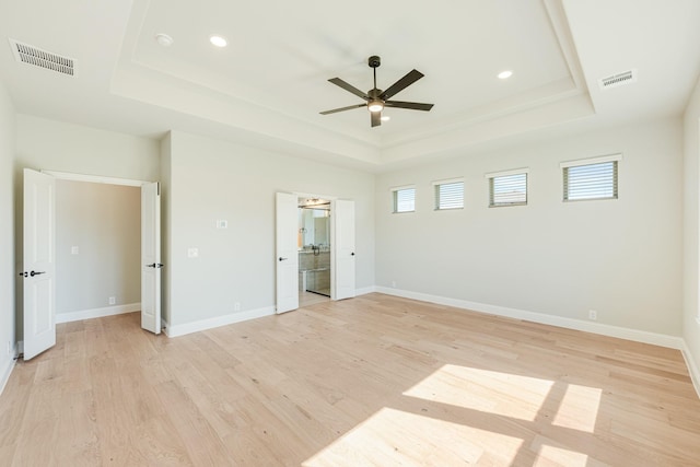 unfurnished bedroom with visible vents, light wood finished floors, baseboards, and a tray ceiling