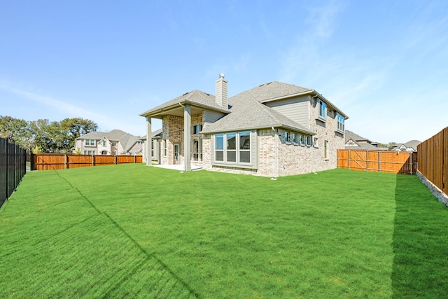 back of house featuring a lawn, a fenced backyard, brick siding, and a chimney
