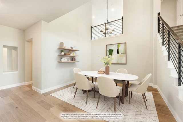 dining space featuring an inviting chandelier, light hardwood / wood-style flooring, and a high ceiling