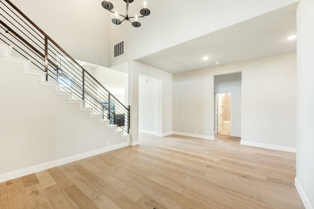 unfurnished living room featuring a towering ceiling, an inviting chandelier, and light wood-type flooring