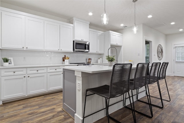 kitchen with white cabinetry, hanging light fixtures, stainless steel appliances, dark hardwood / wood-style floors, and a kitchen island