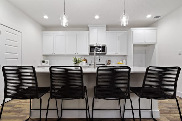 kitchen with white cabinets, hanging light fixtures, and an island with sink