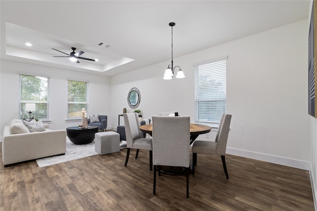 dining area featuring dark hardwood / wood-style floors, ceiling fan with notable chandelier, a wealth of natural light, and a tray ceiling