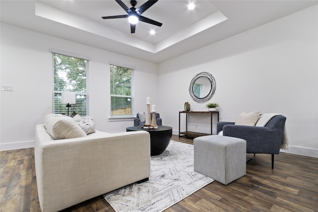 living room with dark hardwood / wood-style flooring, a tray ceiling, and ceiling fan