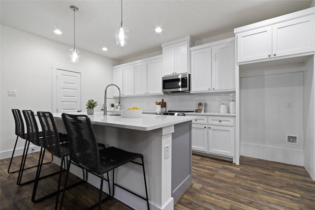 kitchen with dark hardwood / wood-style flooring, decorative light fixtures, a center island with sink, white cabinets, and a breakfast bar area