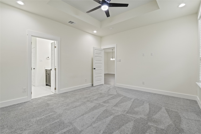 unfurnished bedroom featuring ensuite bathroom, ceiling fan, light carpet, and a tray ceiling