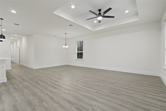 empty room with a raised ceiling, ceiling fan with notable chandelier, and light hardwood / wood-style flooring