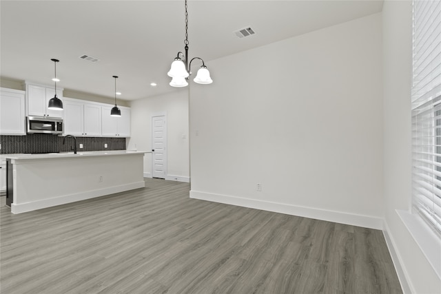 kitchen featuring backsplash, an island with sink, light hardwood / wood-style floors, decorative light fixtures, and white cabinets