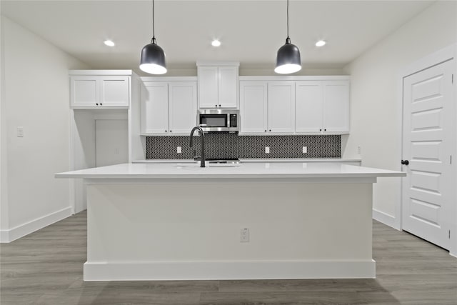 kitchen with light hardwood / wood-style floors, a kitchen island with sink, and hanging light fixtures