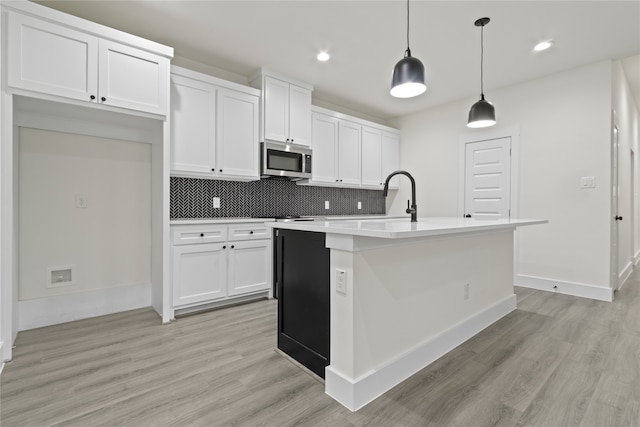 kitchen with pendant lighting, light hardwood / wood-style floors, white cabinets, and a kitchen island with sink