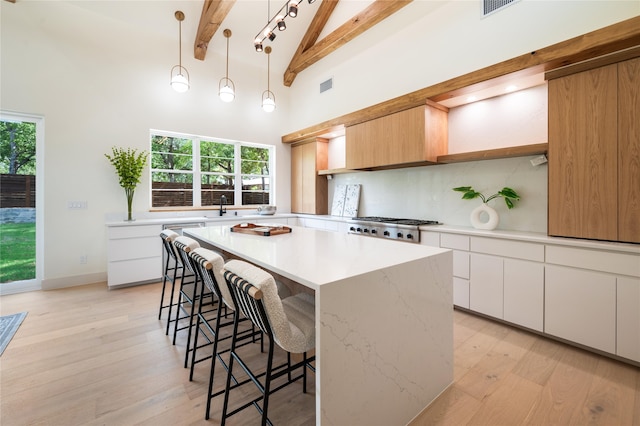 kitchen with a wealth of natural light, beamed ceiling, white cabinetry, and light hardwood / wood-style floors