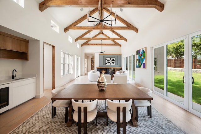 dining area featuring beam ceiling, high vaulted ceiling, light hardwood / wood-style flooring, a notable chandelier, and sink