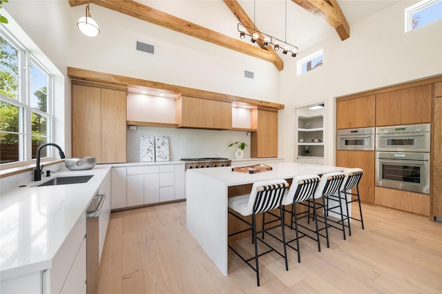 kitchen with beamed ceiling, sink, decorative light fixtures, white cabinetry, and a towering ceiling