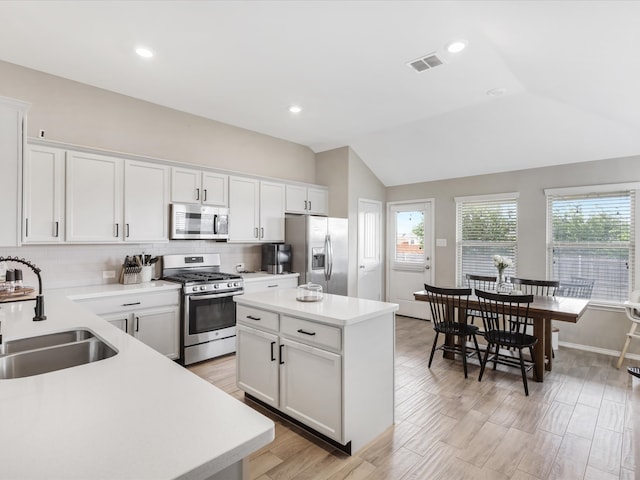 kitchen with white cabinetry, sink, stainless steel appliances, vaulted ceiling, and a kitchen island