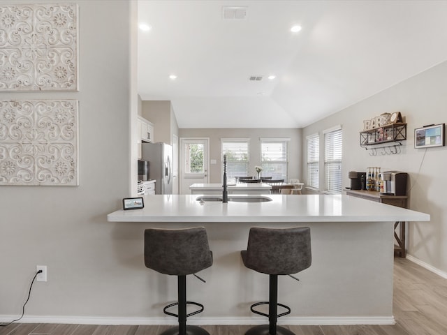 kitchen with stainless steel refrigerator with ice dispenser, kitchen peninsula, vaulted ceiling, a breakfast bar, and light wood-type flooring