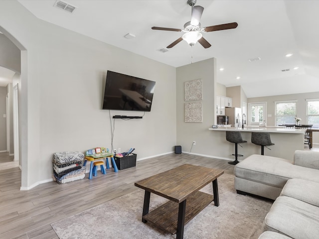 living room featuring ceiling fan, light hardwood / wood-style flooring, and vaulted ceiling