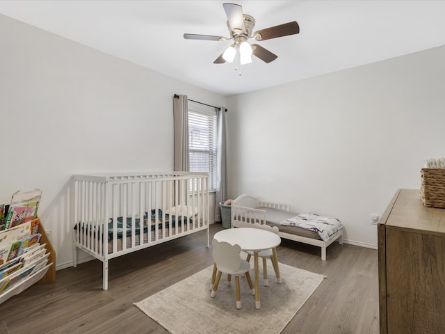 bedroom featuring a crib, ceiling fan, and hardwood / wood-style flooring