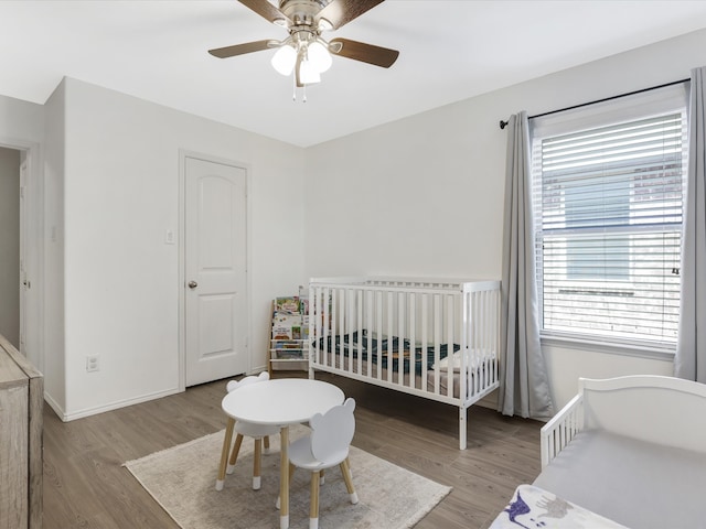 bedroom featuring ceiling fan, light wood-type flooring, and a nursery area