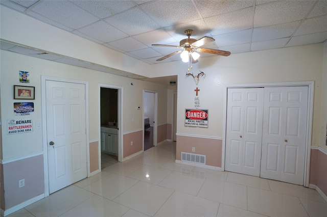 unfurnished bedroom featuring ceiling fan, a drop ceiling, light tile patterned floors, and ensuite bathroom