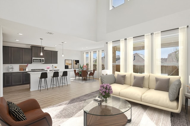 living room featuring sink, light hardwood / wood-style flooring, and a towering ceiling