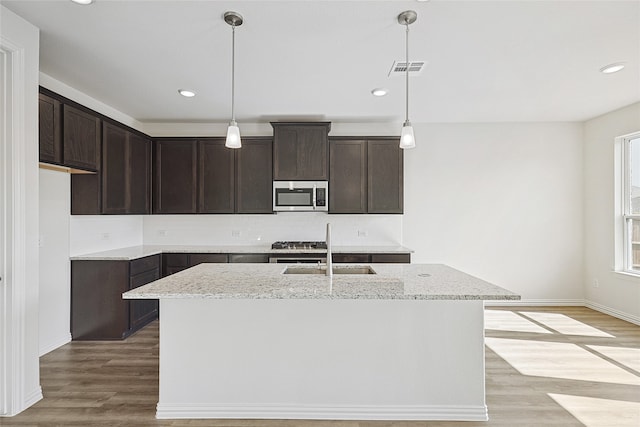 kitchen with appliances with stainless steel finishes, sink, light hardwood / wood-style floors, and an island with sink