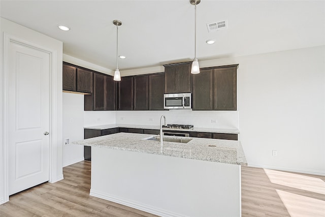 kitchen with sink, an island with sink, decorative light fixtures, and light hardwood / wood-style floors